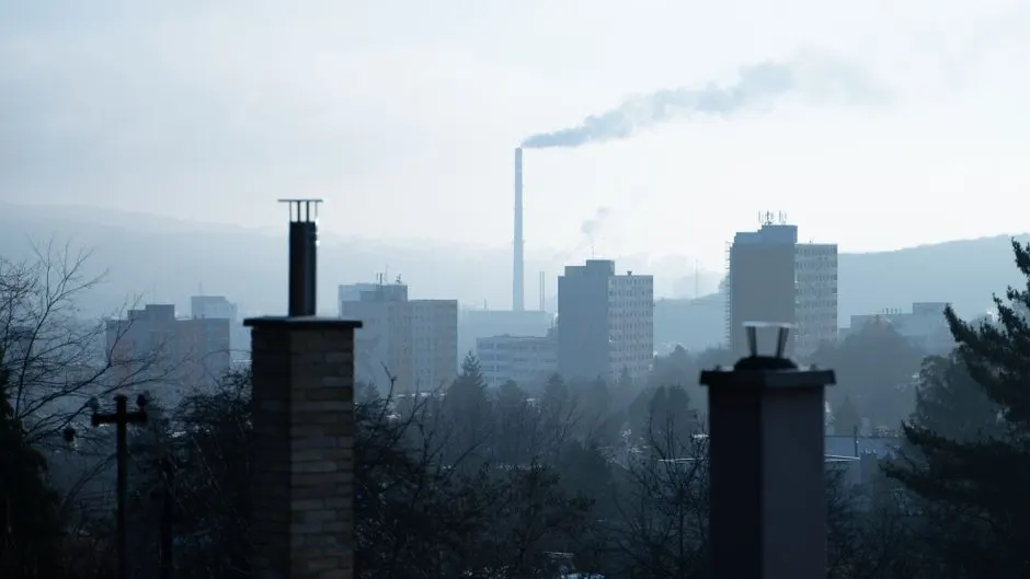 View of an urban landscape with chimneys, smoke, and tall buildings on a foggy day.